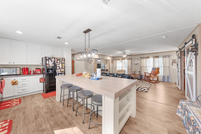 kitchen with light wood finished floors, a barn door, visible vents, black refrigerator with ice dispenser, and white cabinetry