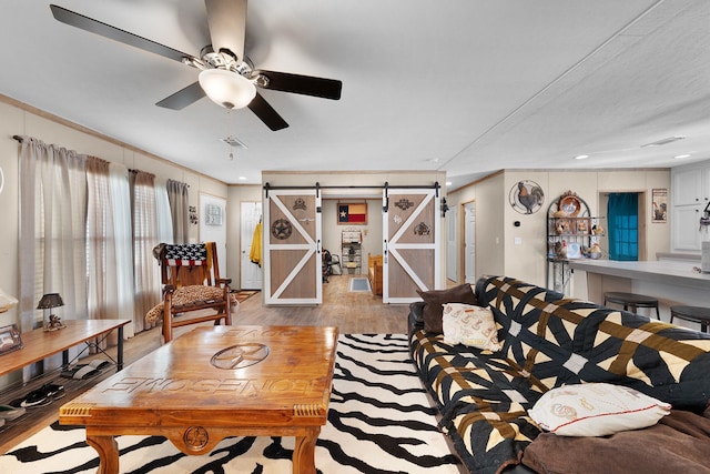 living room with light wood finished floors, recessed lighting, visible vents, a barn door, and a ceiling fan