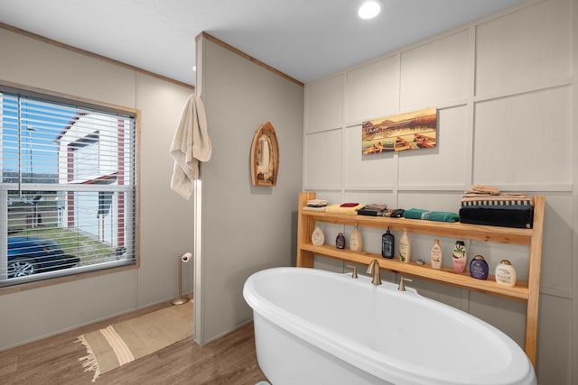 full bath featuring a soaking tub, ornamental molding, a decorative wall, and wood finished floors