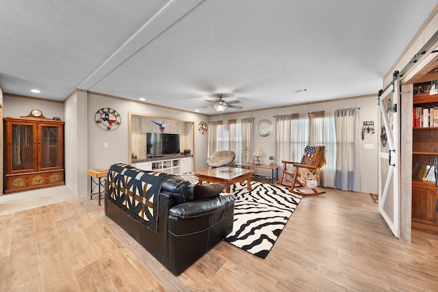 living area with ceiling fan, a barn door, recessed lighting, wood finished floors, and ornamental molding