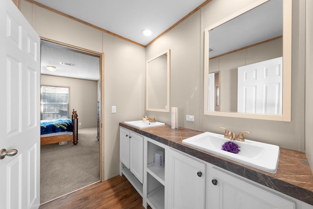 ensuite bathroom featuring wood finished floors, a sink, visible vents, and crown molding