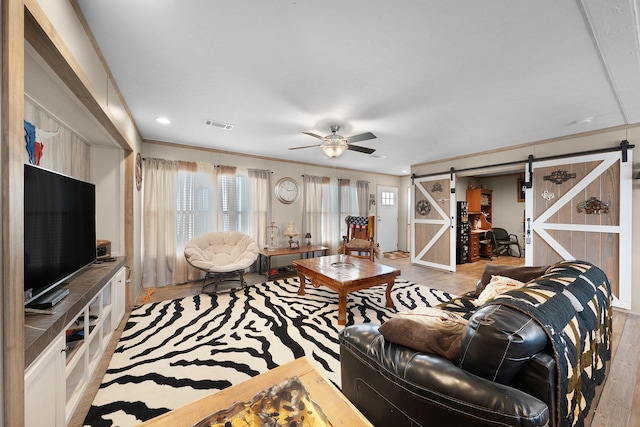 living room with a barn door, visible vents, a ceiling fan, wood finished floors, and crown molding