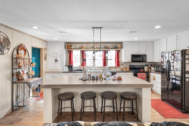 kitchen featuring black appliances, white cabinetry, visible vents, and a kitchen breakfast bar