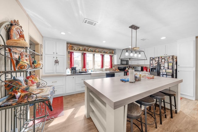 kitchen with visible vents, white cabinets, a center island, black appliances, and light wood finished floors