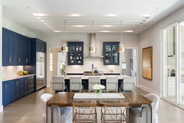 kitchen with light countertops, a kitchen island with sink, a sink, built in appliances, and blue cabinets