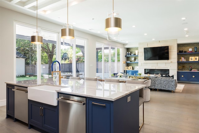 kitchen with blue cabinets, a center island with sink, a sink, and stainless steel dishwasher