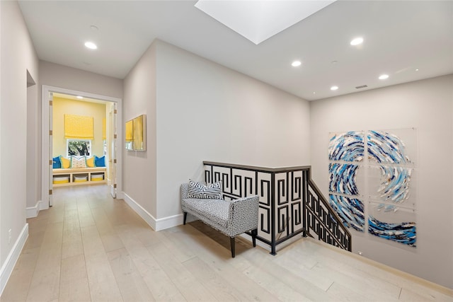 corridor featuring a skylight, baseboards, wood finished floors, an upstairs landing, and recessed lighting