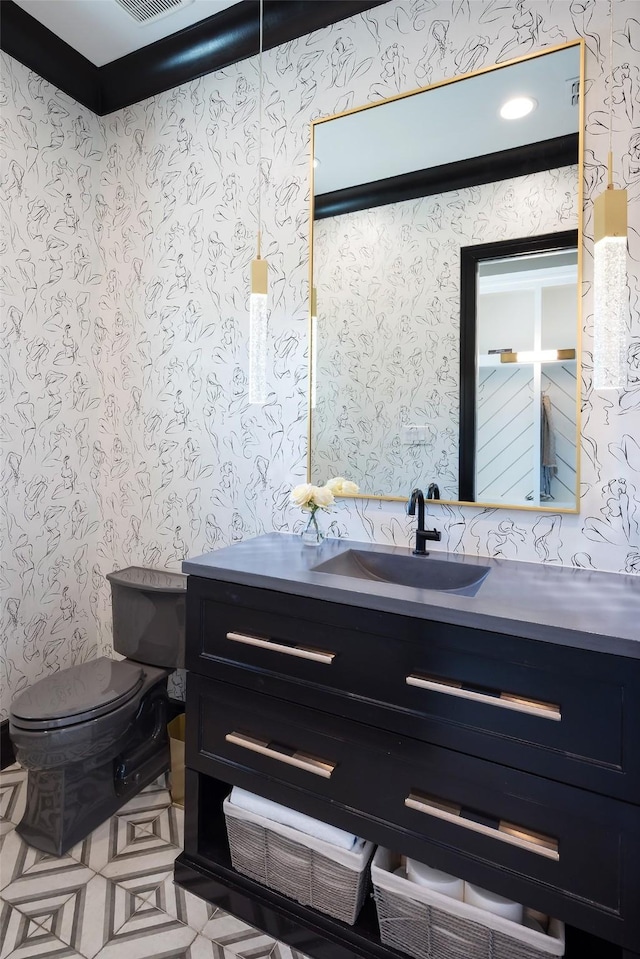 half bathroom featuring visible vents, vanity, toilet, and wallpapered walls