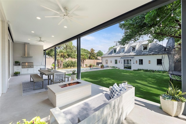 view of patio with a fire pit, an outdoor kitchen, a ceiling fan, area for grilling, and a fenced backyard