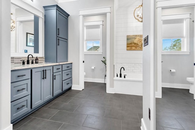 bathroom with a bathtub, a notable chandelier, toilet, vanity, and tile patterned floors