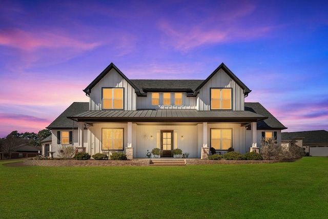 back of house at dusk with a standing seam roof, a yard, a porch, and board and batten siding