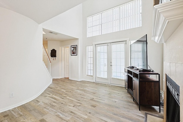 interior space with visible vents, stairs, french doors, light wood-style floors, and a towering ceiling