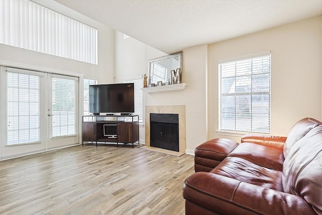 living room with light wood finished floors, plenty of natural light, a tiled fireplace, and a textured ceiling