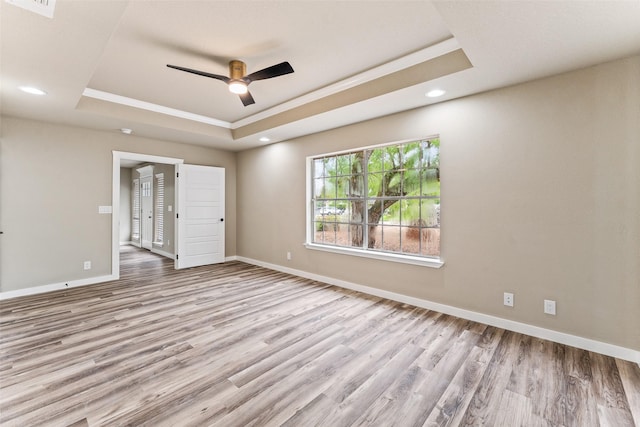 unfurnished bedroom featuring a tray ceiling, recessed lighting, baseboards, and wood finished floors