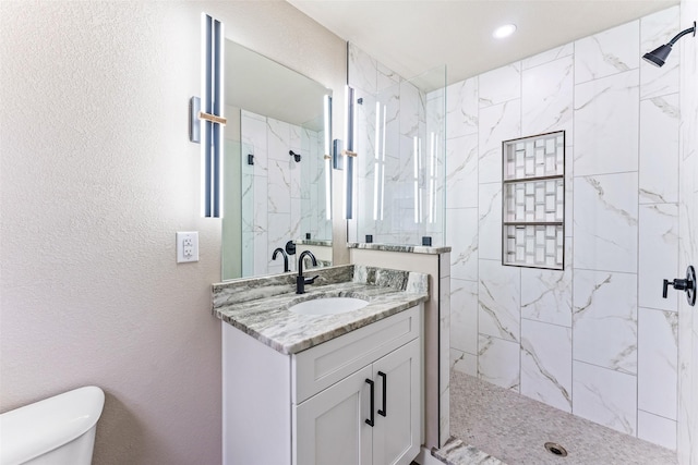 bathroom with toilet, a textured wall, a marble finish shower, and vanity