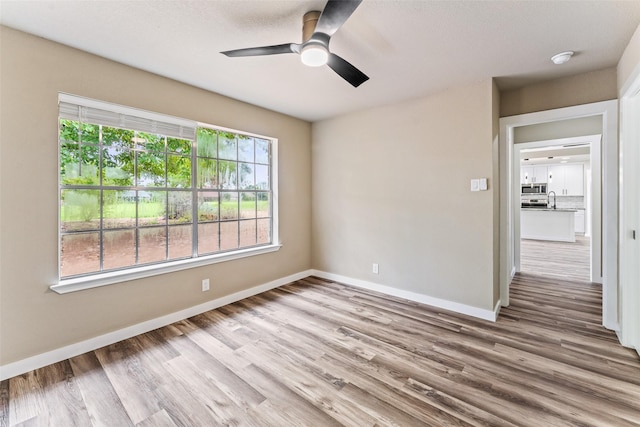 spare room featuring a sink, ceiling fan, baseboards, and wood finished floors