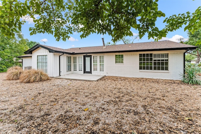 back of property with board and batten siding, brick siding, and a patio