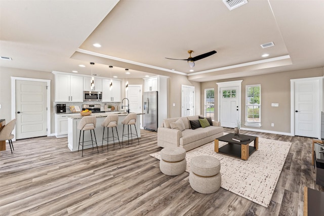 living area featuring light wood-style floors, a tray ceiling, and visible vents