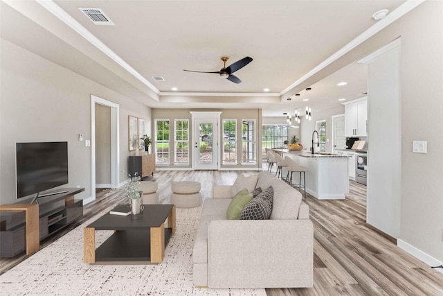 living area featuring a raised ceiling, visible vents, baseboards, and light wood finished floors