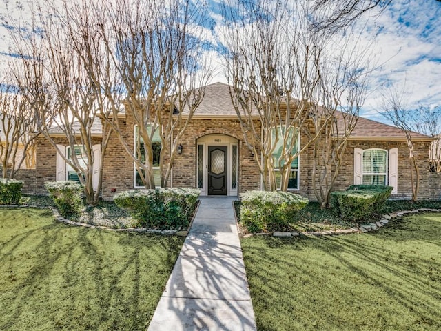 ranch-style home with brick siding, a front yard, and a shingled roof