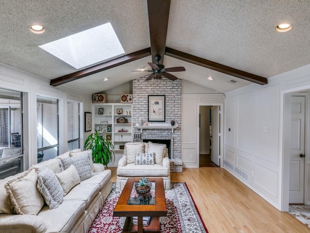 living area featuring light wood finished floors, a decorative wall, lofted ceiling with skylight, a brick fireplace, and a textured ceiling