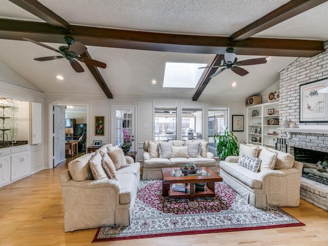 living room with a textured ceiling, vaulted ceiling with skylight, a fireplace, built in features, and light wood-style floors