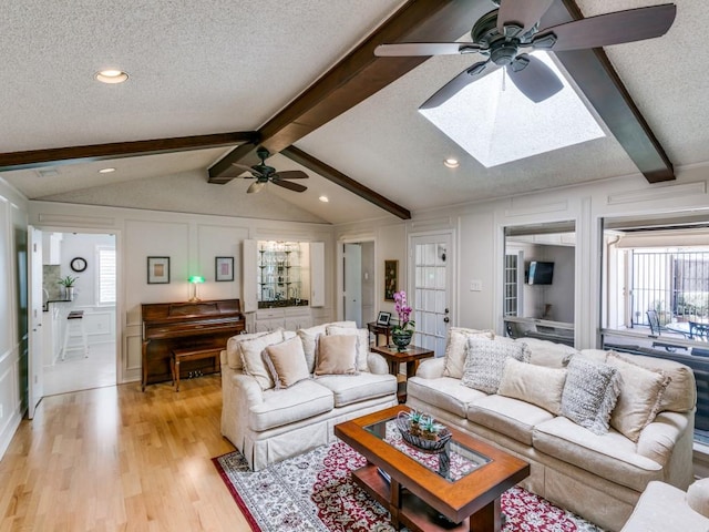 living area with a textured ceiling, lofted ceiling with skylight, light wood-type flooring, and a decorative wall