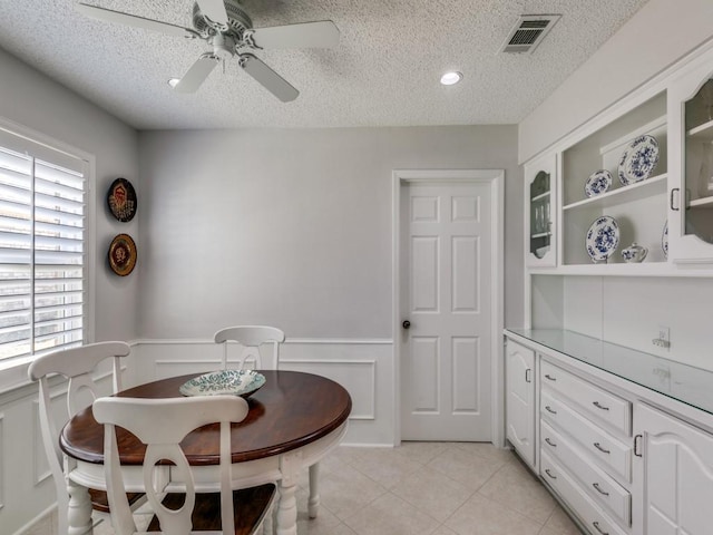 dining room with visible vents, wainscoting, ceiling fan, a textured ceiling, and light tile patterned flooring