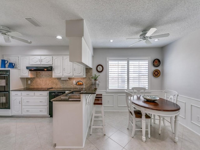 kitchen featuring light tile patterned floors, visible vents, a sink, a peninsula, and under cabinet range hood