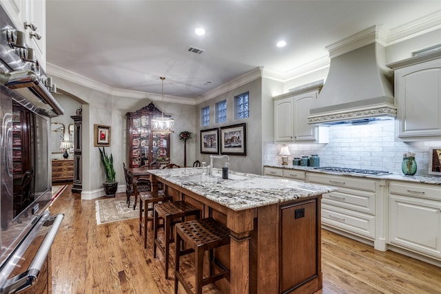 kitchen featuring light wood-style floors, visible vents, custom exhaust hood, and a center island