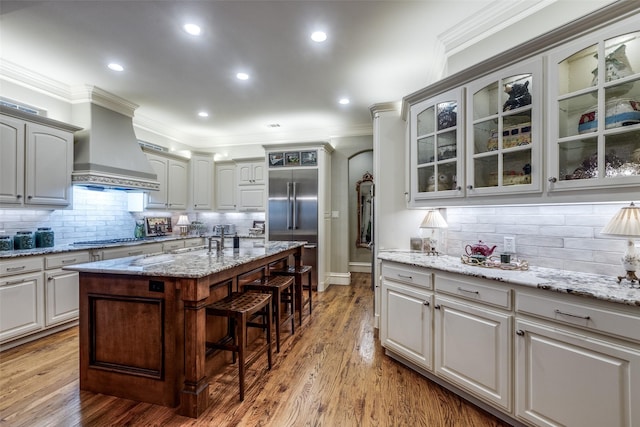 kitchen with crown molding, premium range hood, built in fridge, and a kitchen breakfast bar