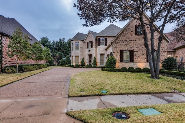 french country inspired facade featuring a front yard, stone siding, brick siding, and concrete driveway