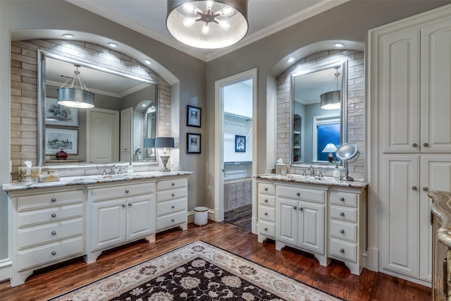 full bath featuring a sink, ornamental molding, two vanities, and wood finished floors