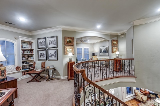 hallway featuring arched walkways, carpet, visible vents, ornamental molding, and an upstairs landing