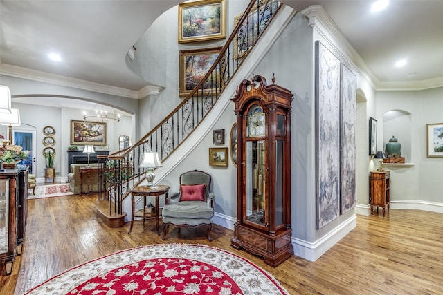 entryway featuring arched walkways, crown molding, stairway, and wood finished floors