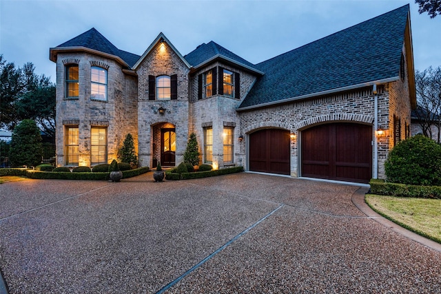 french provincial home with driveway, stone siding, an attached garage, and brick siding