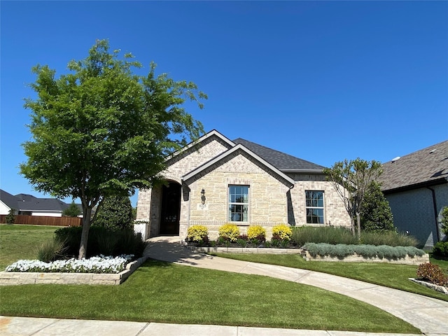 french country style house featuring a shingled roof, a front yard, brick siding, and fence