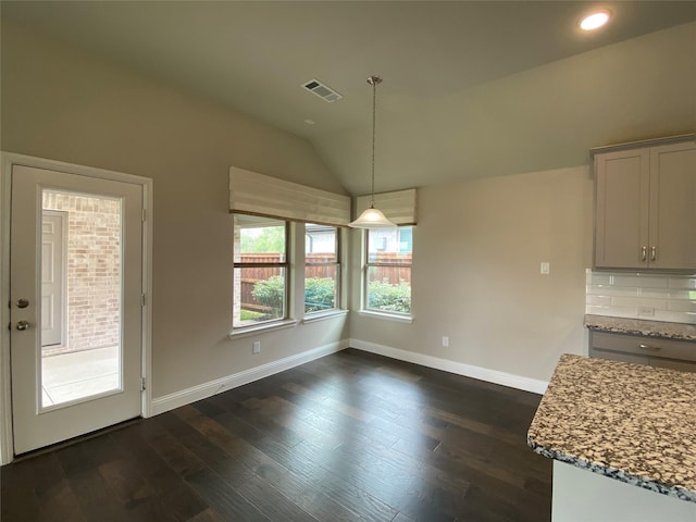 unfurnished dining area with dark wood-style floors, lofted ceiling, visible vents, and baseboards