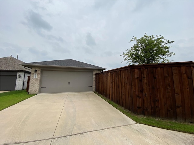 view of side of property featuring roof with shingles, brick siding, an attached garage, fence, and driveway