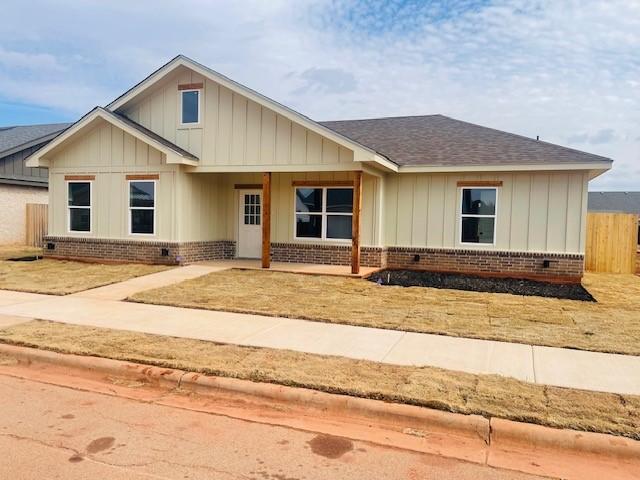 view of front of property with roof with shingles, brick siding, board and batten siding, and fence