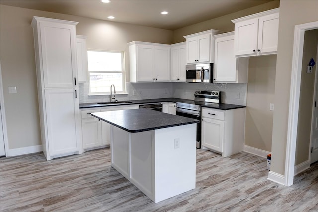 kitchen with stainless steel appliances, dark countertops, a sink, and white cabinetry