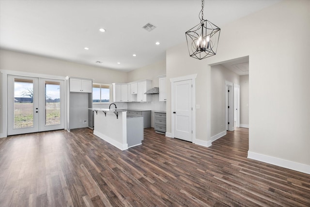 kitchen with dark wood-style flooring, french doors, a kitchen island with sink, white cabinetry, and baseboards