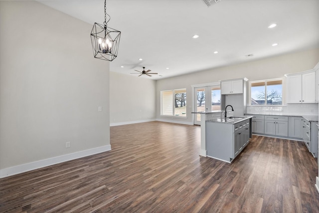 kitchen with backsplash, dark wood-type flooring, open floor plan, a sink, and baseboards