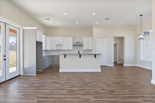 kitchen with dark wood-style floors, french doors, a kitchen island with sink, and decorative backsplash