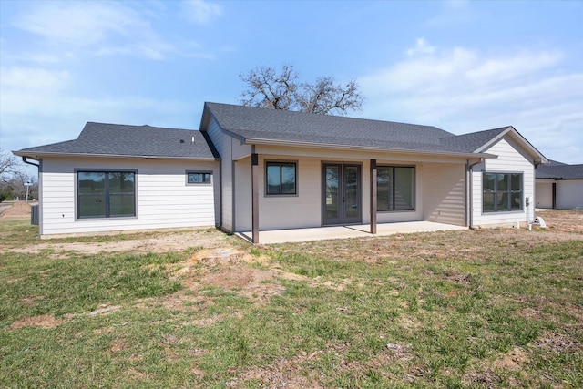 rear view of house featuring roof with shingles, a lawn, and a patio