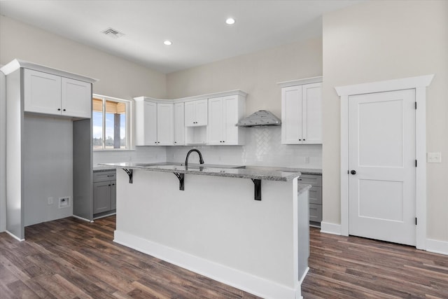 kitchen with visible vents, light stone counters, a kitchen island with sink, a kitchen bar, and backsplash