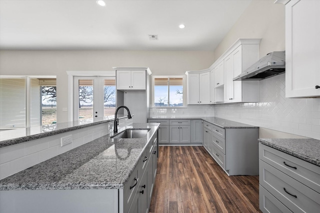 kitchen featuring under cabinet range hood, light stone counters, decorative backsplash, and a sink