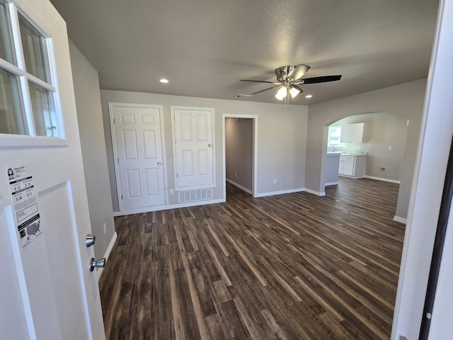 unfurnished bedroom with arched walkways, dark wood-style flooring, recessed lighting, visible vents, and baseboards