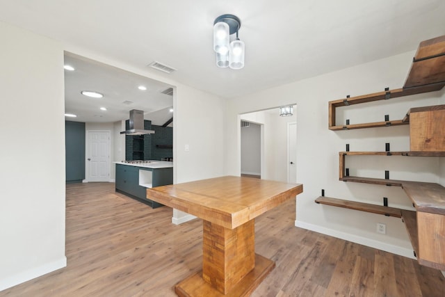 kitchen with light wood-style flooring, visible vents, wall chimney range hood, and open shelves