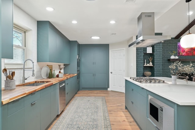 kitchen featuring butcher block counters, range hood, stainless steel appliances, light wood-type flooring, and a sink